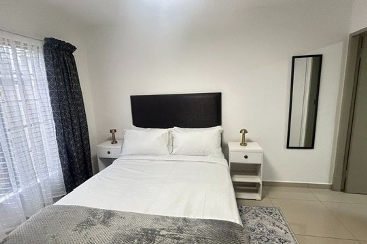 A well-maintained bedroom featuring neutral tiled flooring, clean white walls, and a large window allowing for natural light.