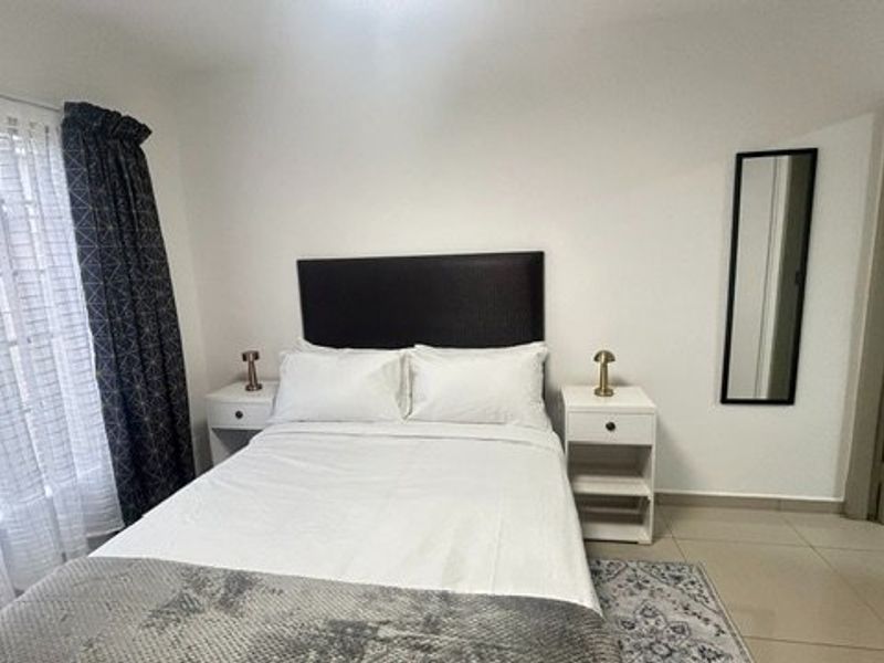 A well-maintained bedroom featuring neutral tiled flooring, clean white walls, and a large window allowing for natural light.