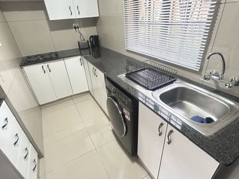 A compact, functional kitchen featuring granite countertops, white cabinetry, tiled splashbacks, and a stainless steel sink with a mixer tap.