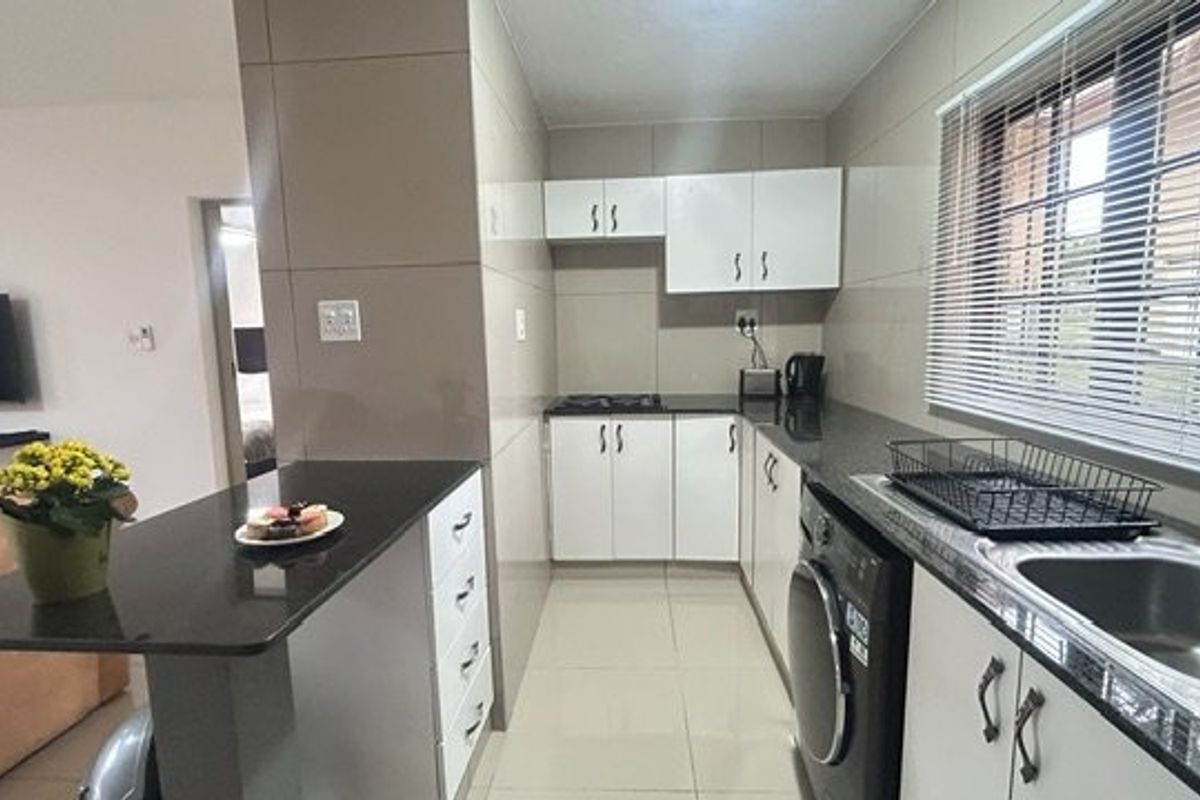 A functional kitchen featuring granite countertops, white cabinetry, tiled walls, and a built-in hob, with an integrated breakfast bar area.