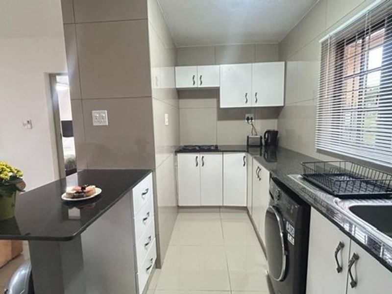 A functional kitchen featuring granite countertops, white cabinetry, tiled walls, and a built-in hob, with an integrated breakfast bar area.