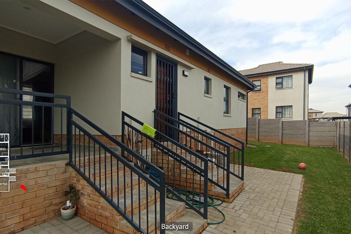 Rear exterior view of the house featuring a paved patio area, concrete stairs with metal railings, and a private garden with boundary walling.