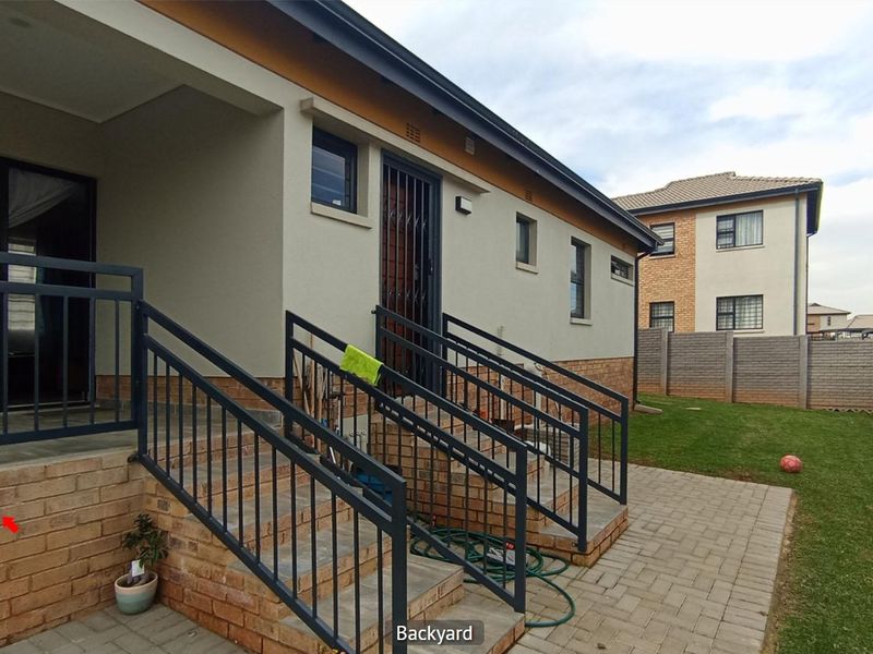 Rear exterior view of the house featuring a paved patio area, concrete stairs with metal railings, and a private garden with boundary walling.