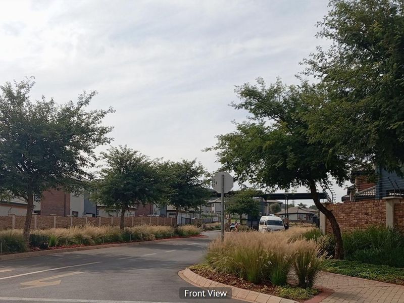 A view of the street approach featuring paved roads, sidewalks, and established brick boundary walls within a residential estate setting.
