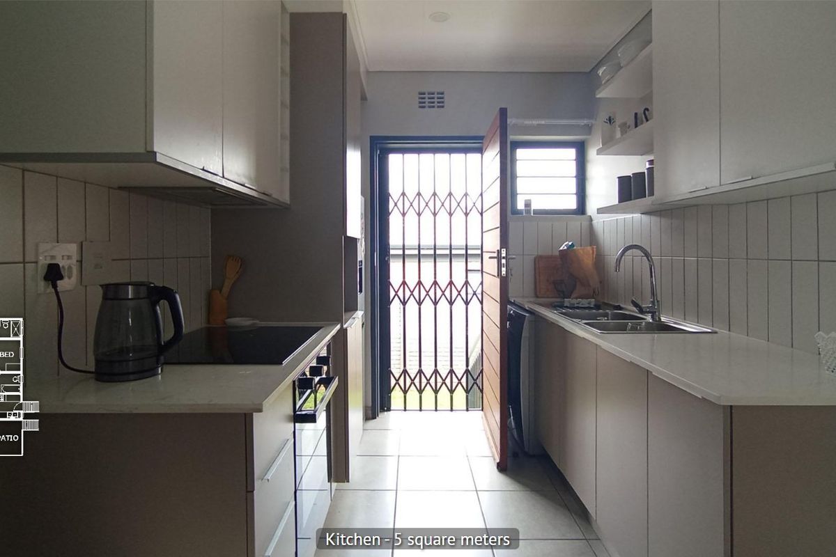 Compact galley-style kitchen featuring modern cabinetry, built-in oven and hob, stainless steel sink, and direct access to the exterior via a security gate.