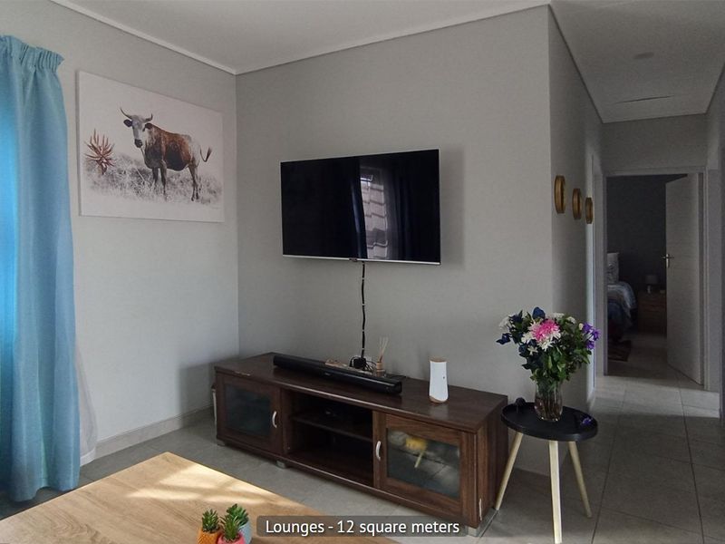 A compact living room featuring neutral wall tones, tiled flooring, and a wall-mounted television setup, providing a functional and well-maintained space.