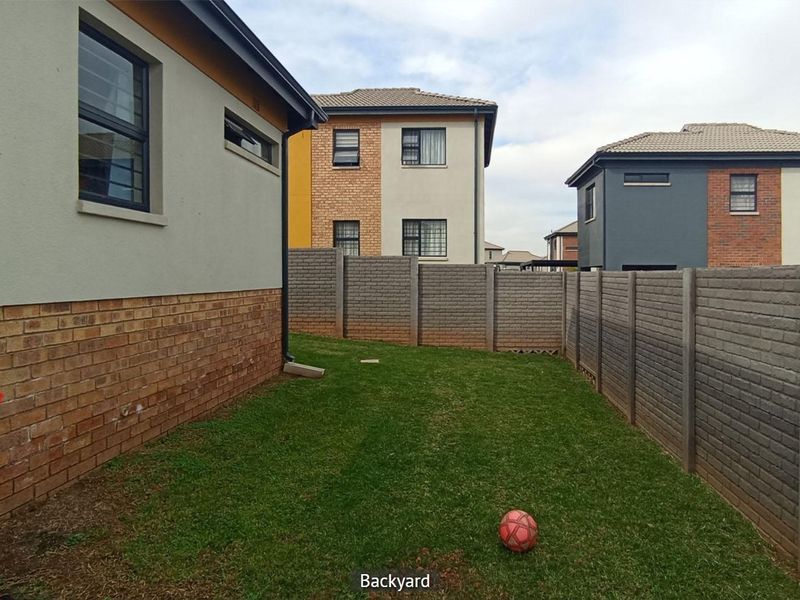 A private rear garden featuring a well-maintained lawn enclosed by precast concrete boundary walls and adjacent to the brick and plaster house exterior.