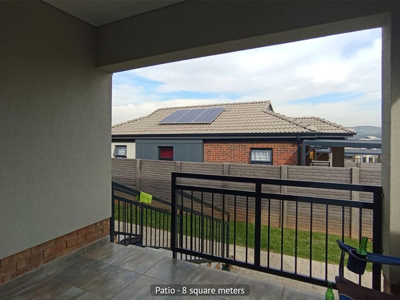 A covered patio area featuring tiled flooring and a metal balustrade, overlooking a private garden and boundary wall.