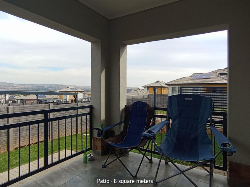 A covered patio area featuring tiled flooring and a metal balustrade, offering an open view of the surrounding residential estate.