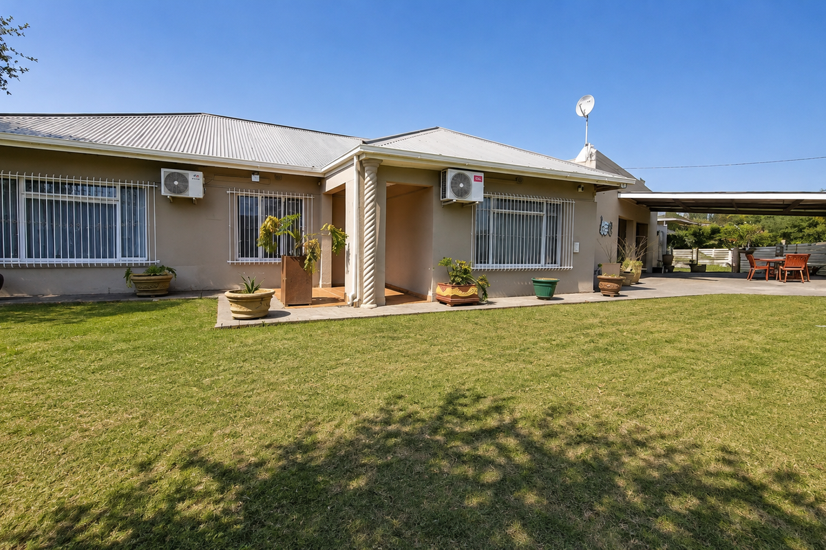 Rear view of the house featuring a spacious lawn, covered patio area, and exterior wall-mounted air conditioning units.