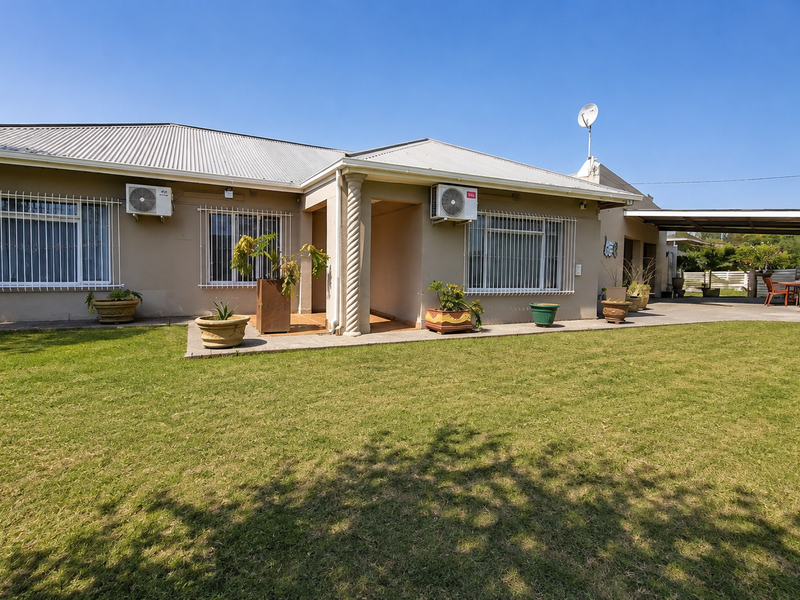 Rear view of the house featuring a spacious lawn, covered patio area, and exterior wall-mounted air conditioning units.