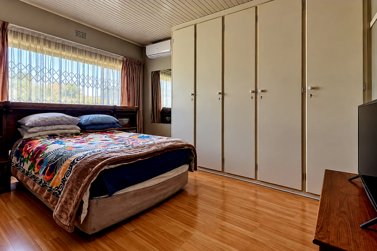 A well-maintained bedroom featuring extensive built-in cabinetry, laminate flooring, and a split-system air conditioner for climate control.