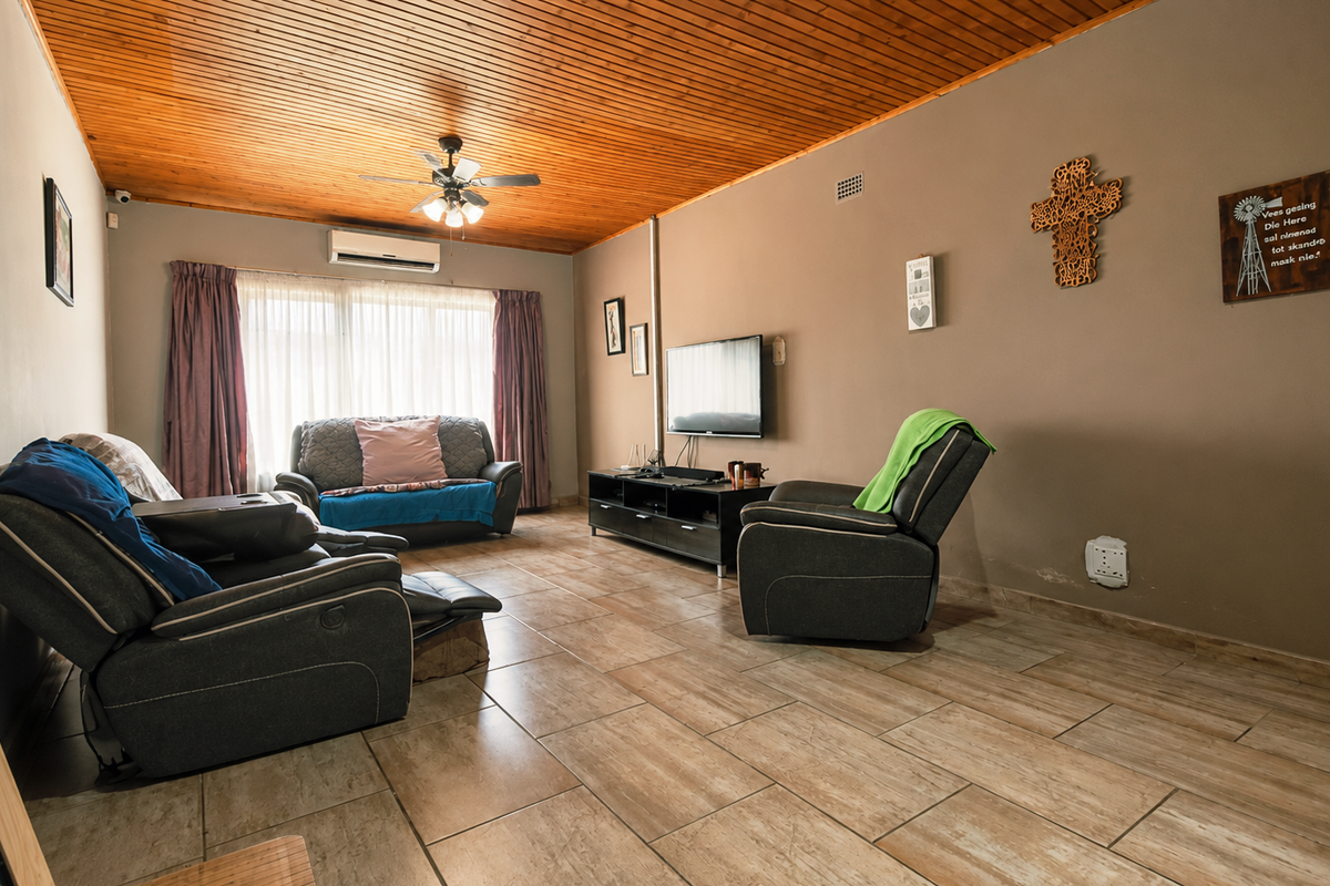 A living room featuring a timber tongue and groove ceiling, ceramic tiled flooring, and a wall-mounted split system air conditioner.