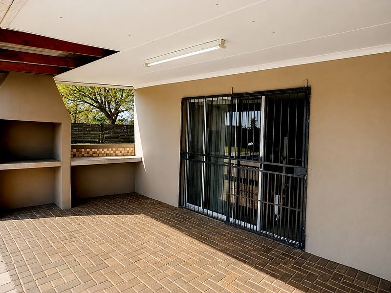 Covered patio area featuring a built-in braai, paved flooring, and a security gate, providing a functional outdoor entertainment space.