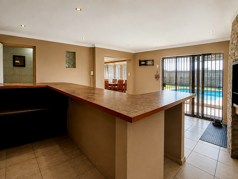 Spacious entertainment area featuring a built-in bar, stone-clad fireplace, and direct access to the outdoor pool area through sliding glass doors.