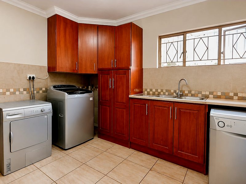 Functional laundry room featuring wooden cabinetry, tiled splashback, stainless steel sink, and dedicated space for laundry appliances.