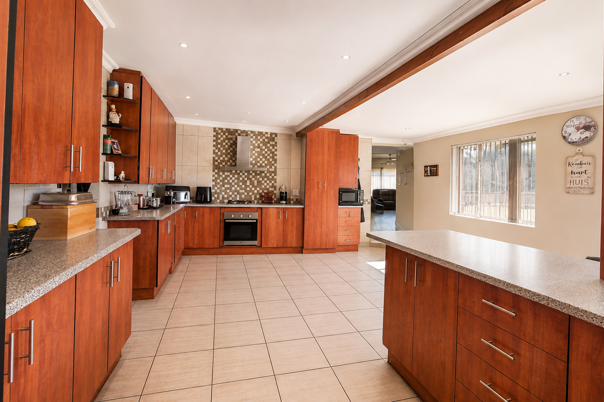 Spacious open-plan kitchen featuring warm-toned wooden cabinetry, granite countertops, stainless steel appliances, and tiled flooring, seamlessly connecting to the adjacent living area.