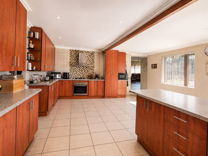 Spacious open-plan kitchen featuring warm-toned wooden cabinetry, granite countertops, stainless steel appliances, and tiled flooring, seamlessly connecting to the adjacent living area.