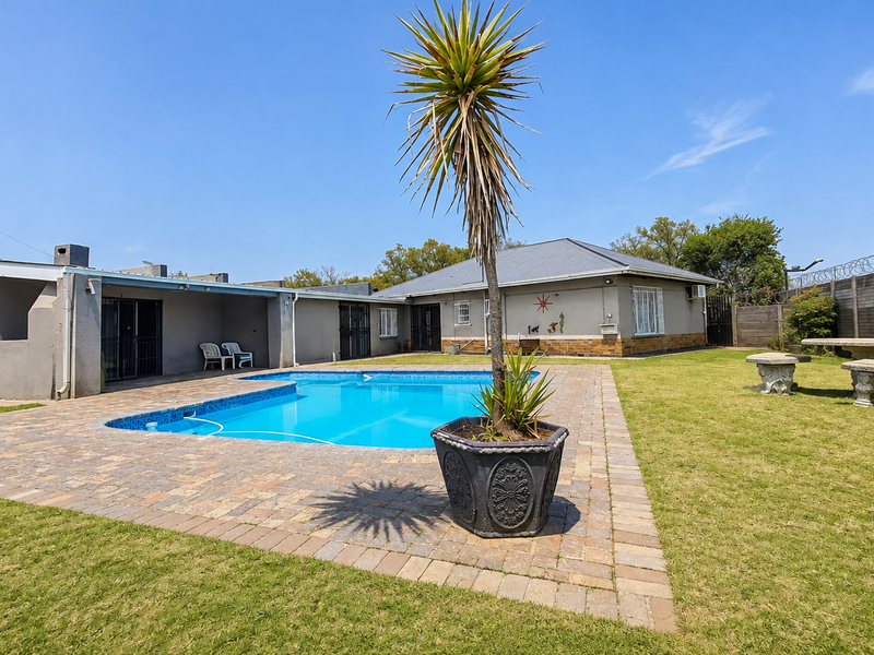 A spacious rear garden featuring a swimming pool with a paved surround, covered patio area, and secure perimeter fencing.