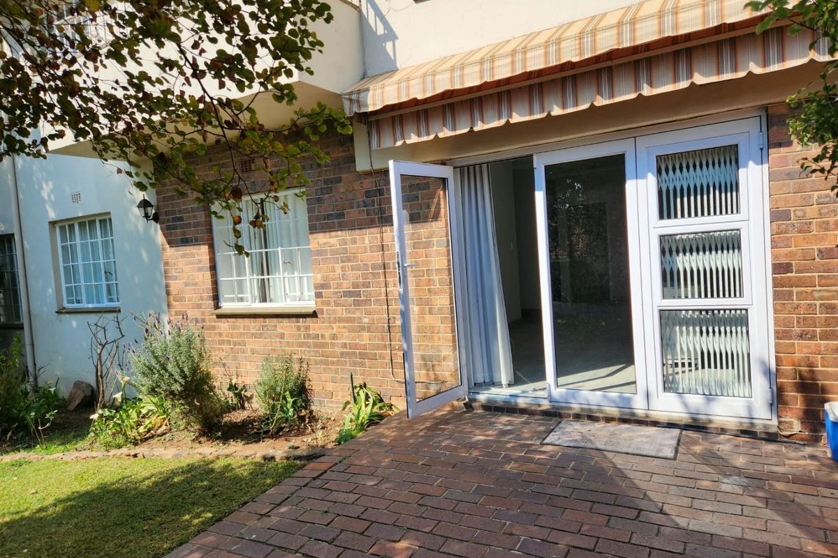 Rear exterior view of the townhouse featuring a brick-paved patio, retractable awning, and secure glass sliding door access to the interior living space.