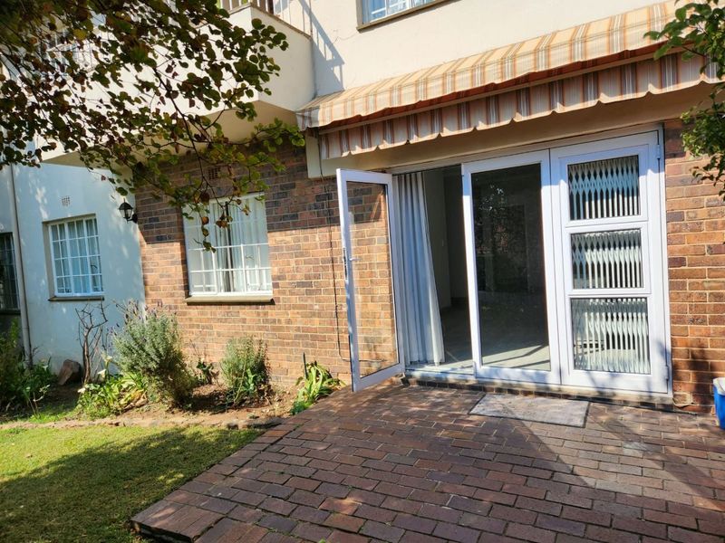 Rear exterior view of the townhouse featuring a brick-paved patio, retractable awning, and secure glass sliding door access to the interior living space.