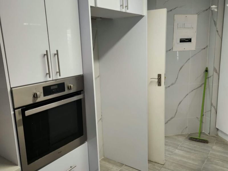 Modern kitchen area featuring high-gloss white cabinetry, built-in oven, marble-effect wall tiling, and neutral floor tiles, presenting a clean and functional space.