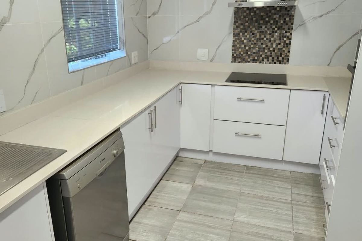 Modern kitchen featuring white cabinetry, stone countertops, marble-look wall tiles, and a stainless steel extractor fan with a mosaic tile feature splashback.