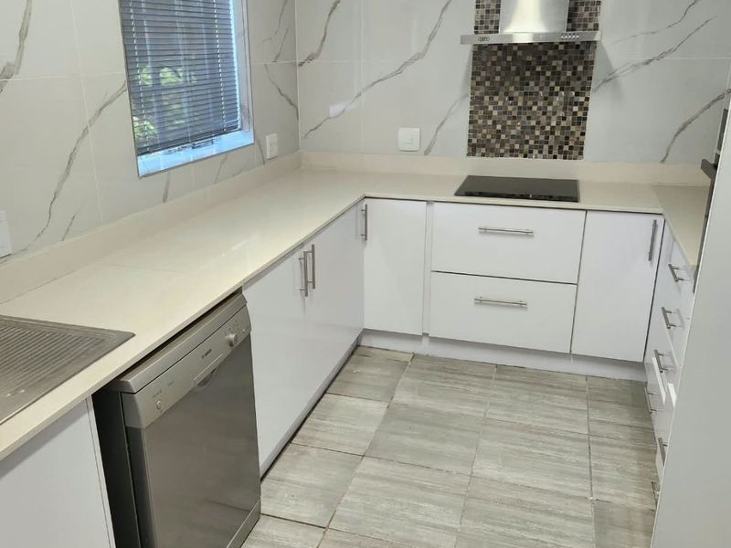 Modern kitchen featuring white cabinetry, stone countertops, marble-look wall tiles, and a stainless steel extractor fan with a mosaic tile feature splashback.
