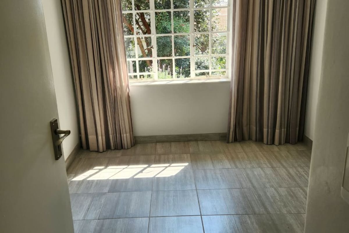 A bright, empty bedroom featuring neutral tiled flooring and a large grid-pattern window with floor-to-ceiling curtains.