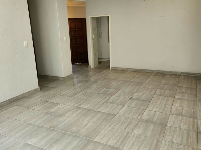 A spacious, empty living area featuring neutral tiled flooring, coved ceilings, and a central light fixture, providing a blank canvas for interior design.