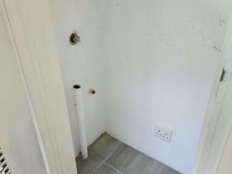 A compact laundry utility space featuring tiled flooring, plumbing connections for a washing machine, and an electrical outlet.