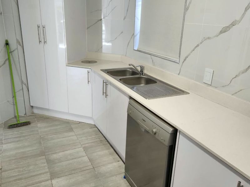 A clean and modern scullery featuring white cabinetry, stone countertops, marble-look wall tiling, and a double bowl stainless steel sink.