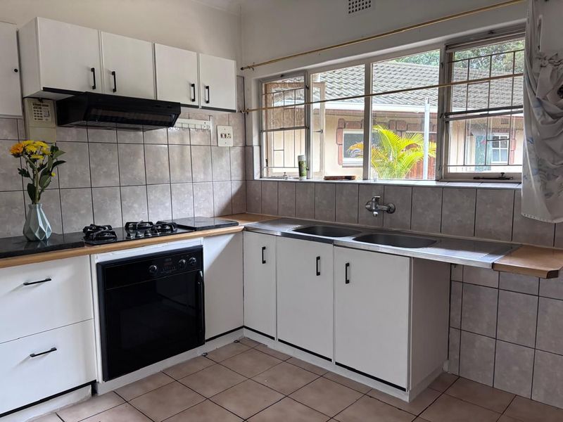 Functional kitchen featuring white cabinetry, gas hob, built-in oven, extractor fan, and double stainless steel sink with tiled splashbacks and flooring.
