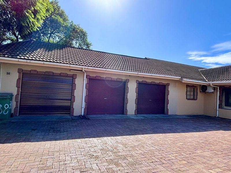 A well-maintained triple garage featuring roller doors, a tiled roof, and a spacious paved driveway area.