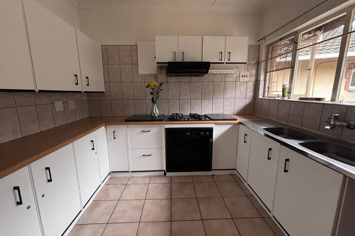 A functional kitchen featuring white cabinetry, laminate countertops, a gas hob with extractor, and a double basin sink with tiled backsplash and flooring.