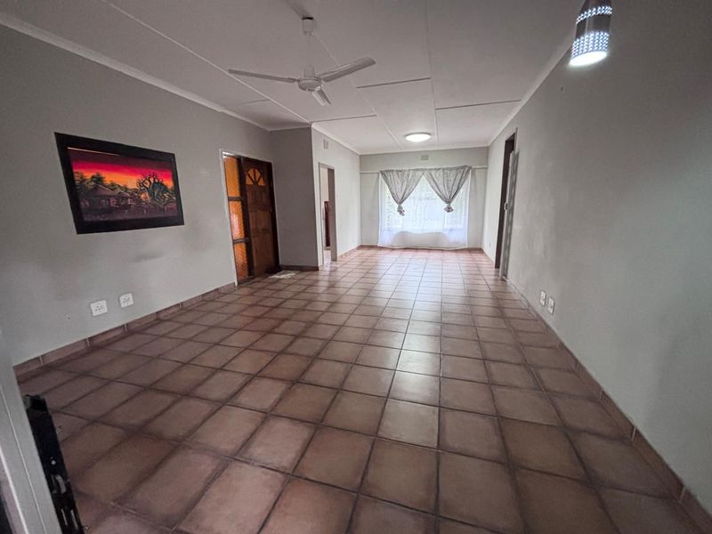 A spacious, empty living area featuring neutral walls, tiled flooring, and a ceiling fan, offering a blank canvas for interior design.