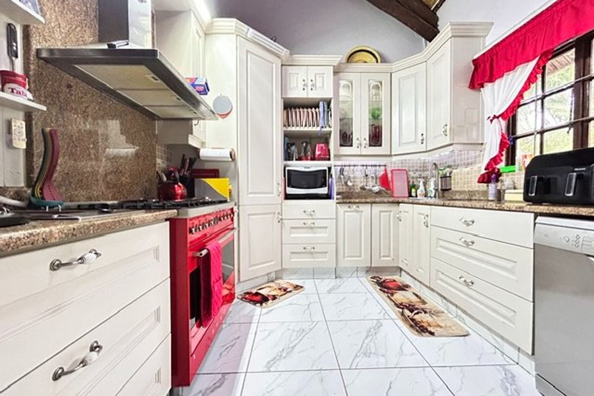 A well-appointed kitchen featuring cream cabinetry, granite countertops, a striking red stove, and high-quality tiled flooring under exposed timber ceiling beams.