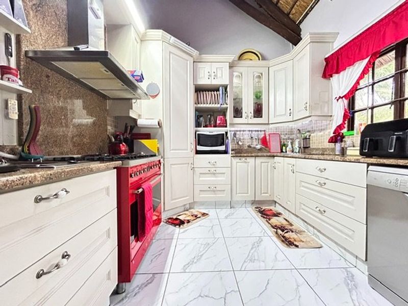 A well-appointed kitchen featuring cream cabinetry, granite countertops, a striking red stove, and high-quality tiled flooring under exposed timber ceiling beams.