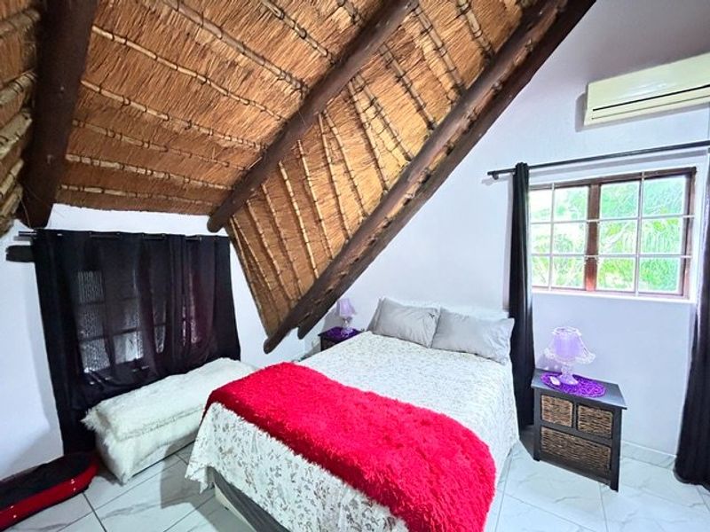 A bedroom featuring a unique exposed thatch roof with timber rafters, tiled flooring, and a wall-mounted air conditioning unit.
