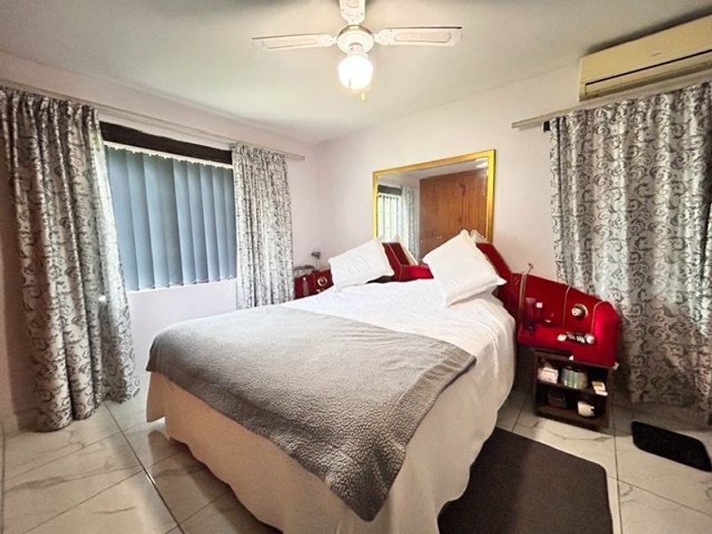 A bedroom featuring tiled flooring, a ceiling fan, and a wall-mounted air conditioning unit.