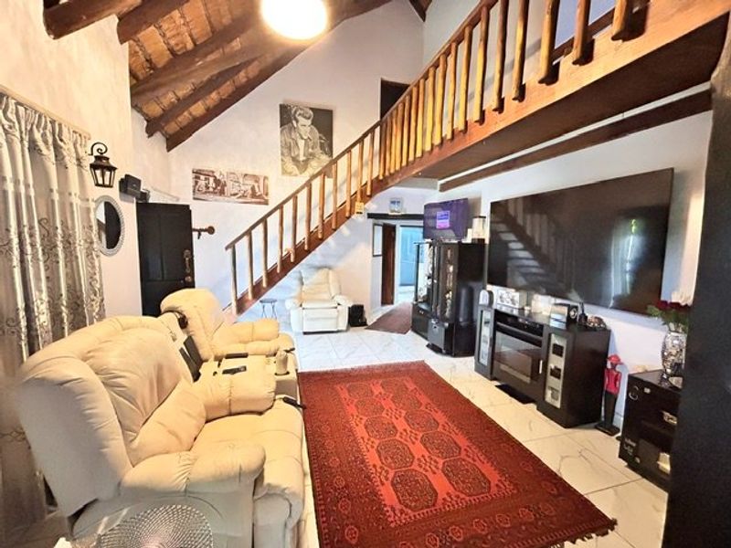 Spacious living room featuring a vaulted ceiling with exposed timber beams, a wooden staircase leading to a mezzanine level, and tiled flooring.