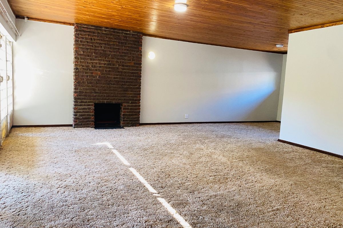 Spacious living room featuring a classic brick fireplace, timber-clad ceiling, and neutral carpeting, offering a blank canvas for modern interior updates.