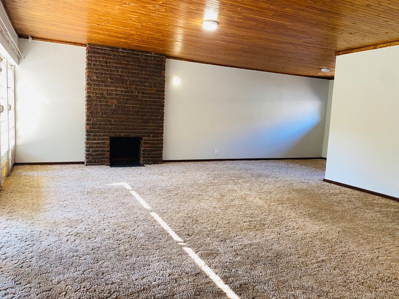 Spacious living room featuring a classic brick fireplace, timber-clad ceiling, and neutral carpeting, offering a blank canvas for modern interior updates.