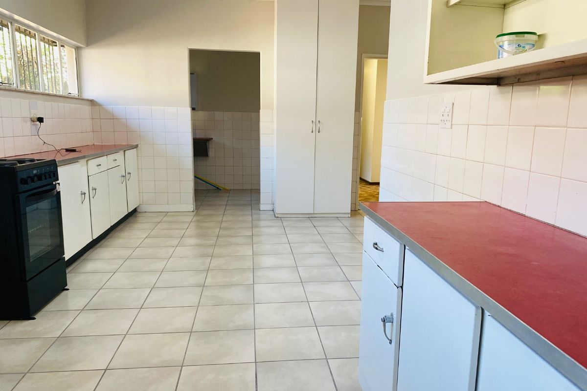 A functional, empty kitchen featuring tiled flooring, white cabinetry, red laminate countertops, and a built-in pantry cupboard, offering potential for modern updates.