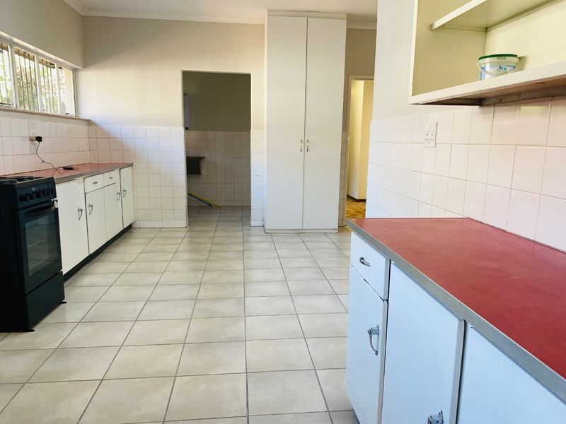 A functional, empty kitchen featuring tiled flooring, white cabinetry, red laminate countertops, and a built-in pantry cupboard, offering potential for modern updates.