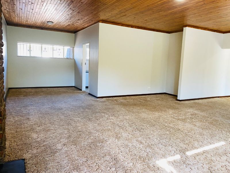 Spacious, empty living area featuring a warm timber tongue and groove ceiling, neutral carpeting, and a brick fireplace surround.
