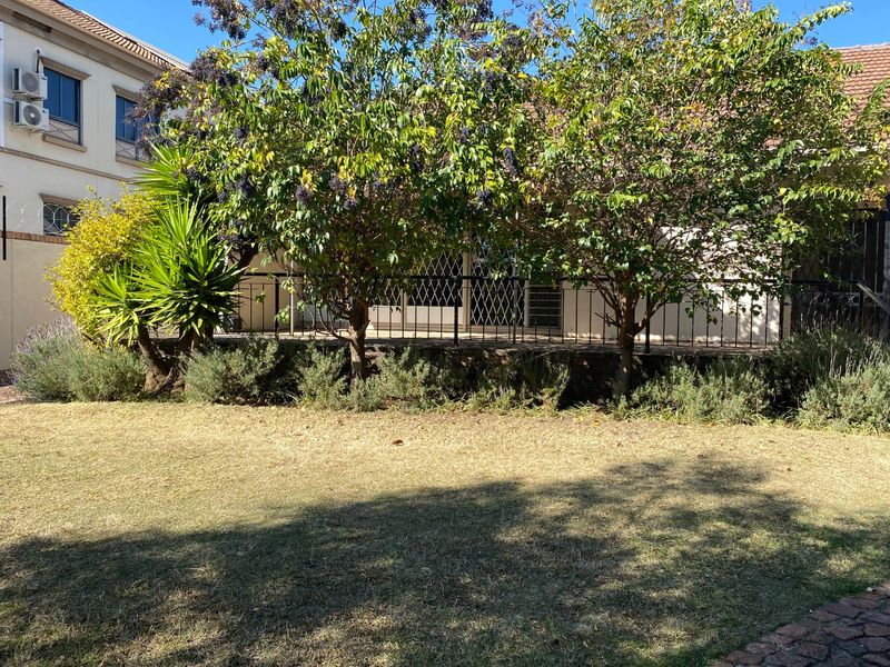 Rear view of the property featuring a paved patio area, security gates, and a garden with established trees and lawn.