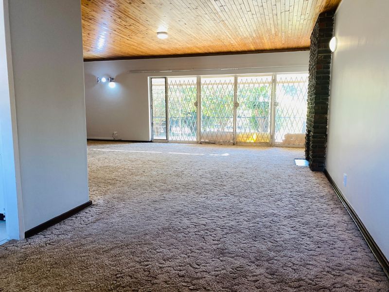 Spacious living area featuring a timber ceiling, brick fireplace, and large sliding glass doors with security gates leading to the exterior.