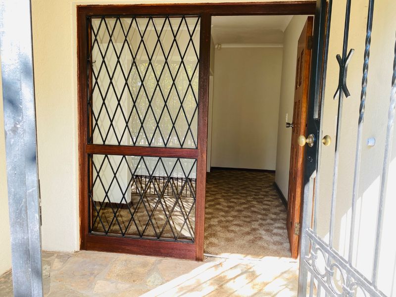 Entrance area featuring a security gate, wooden door with diamond pattern screen, and carpeted flooring leading into the home.