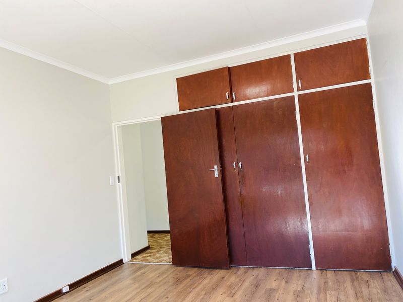 A vacant bedroom featuring laminate flooring and extensive built-in wooden cupboards with overhead storage compartments.